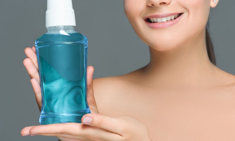 partial view of smiling woman with bare shoulders holding mouthwash isolated on grey