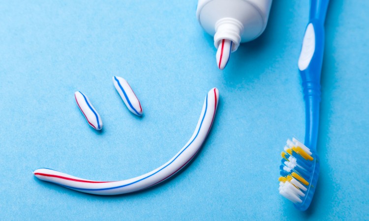 Tooth-paste in the form of face with a smile. Tube of toothpaste and toothbrush on blue background. Refreshing and whitening toothpaste.