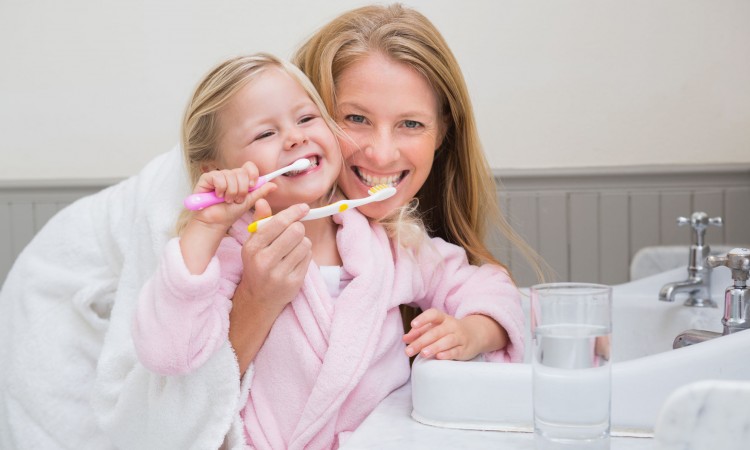 Happy mother and daughter brushing their teeth at home in the bathroom