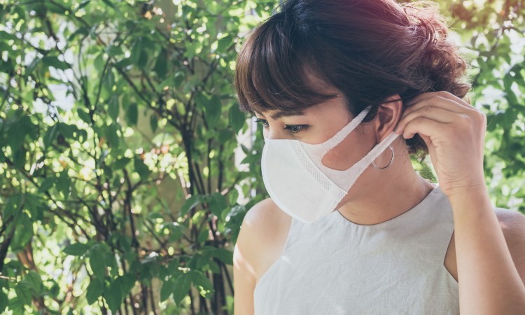 Beautiful asian woman wearing white protective N95 dust mask on green leaves background with copy space. Protection against pollution concept.