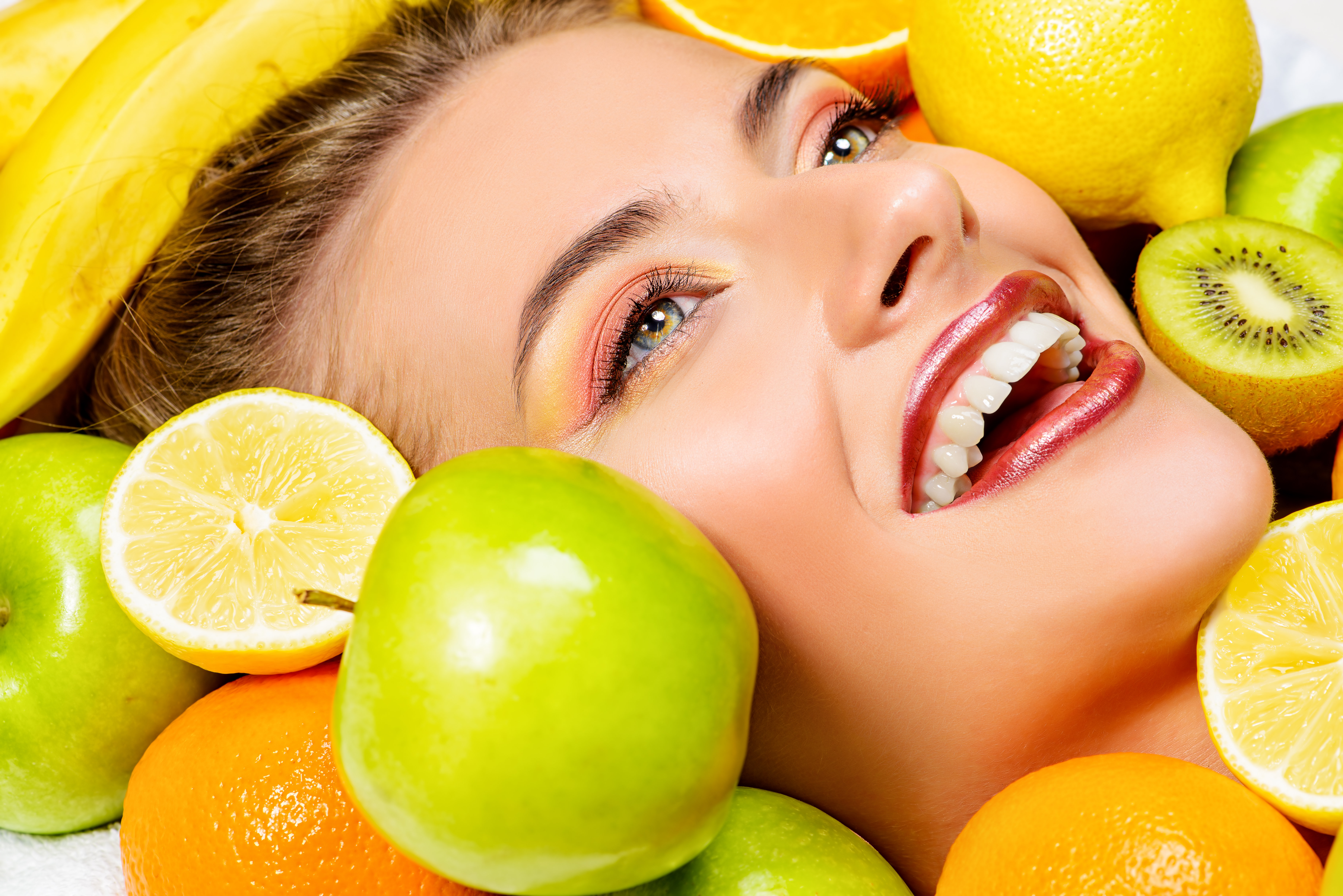 Close-up portrait of a beautiful smiling woman among fresh fruts. Healthy eating, juice. Make-up, cosmetics. Healthy teeth.