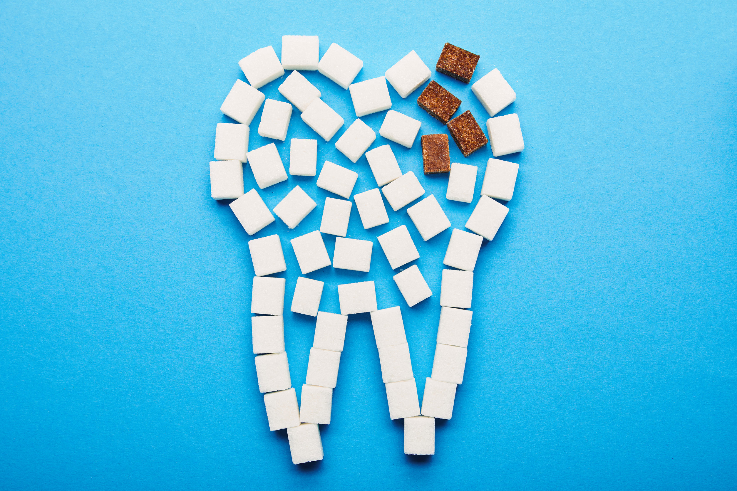 top view of white and brown sugar cubes arranged in tooth sign on blue background, dental caries concept